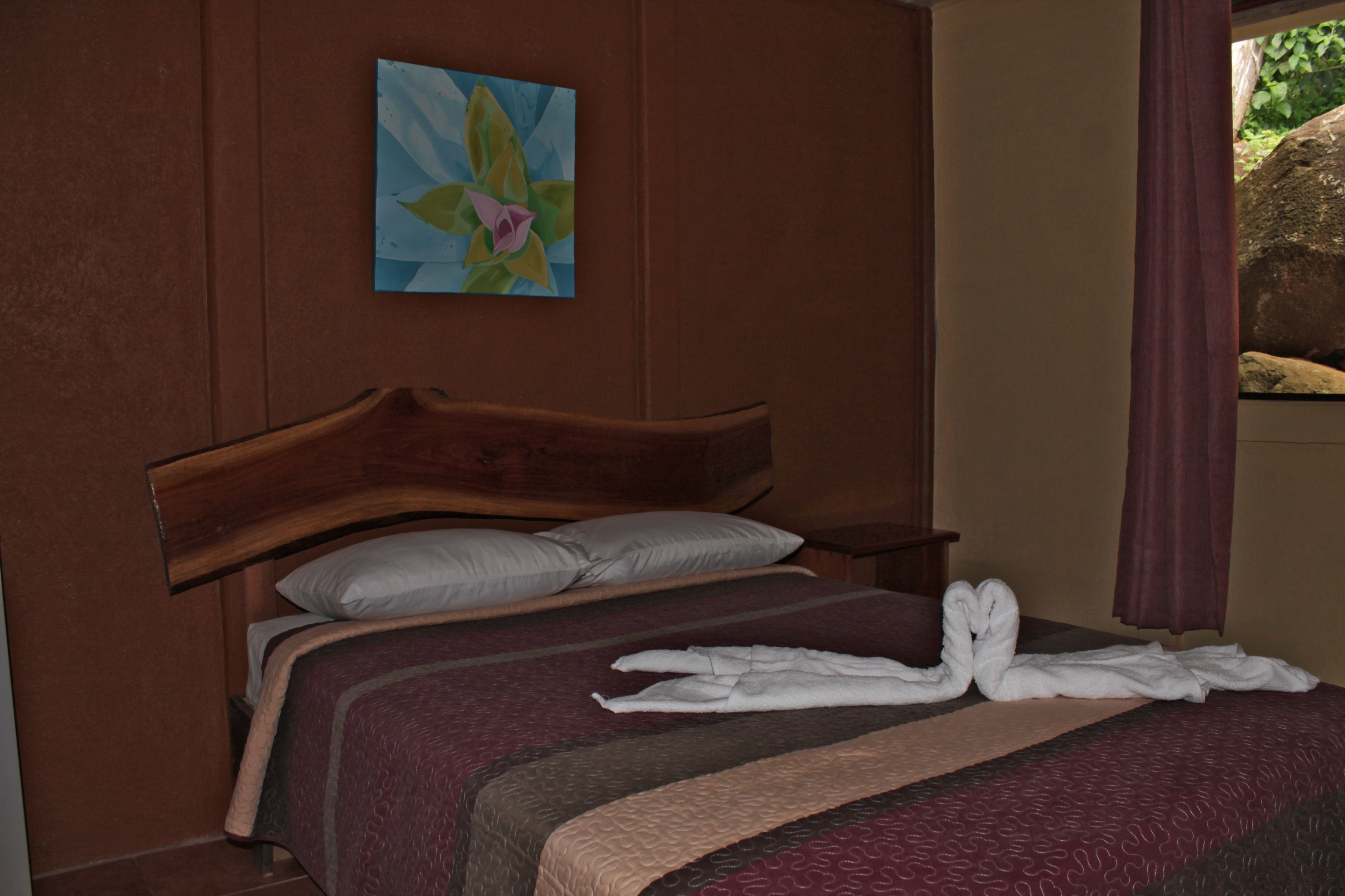 Een hotelkamer met een houten bed, een schilderij aan de muur en een raam met gordijnen.