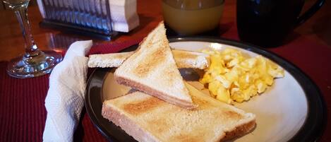 A breakfast plate with toast, scrambled eggs, and a glass of orange juice on a table.
