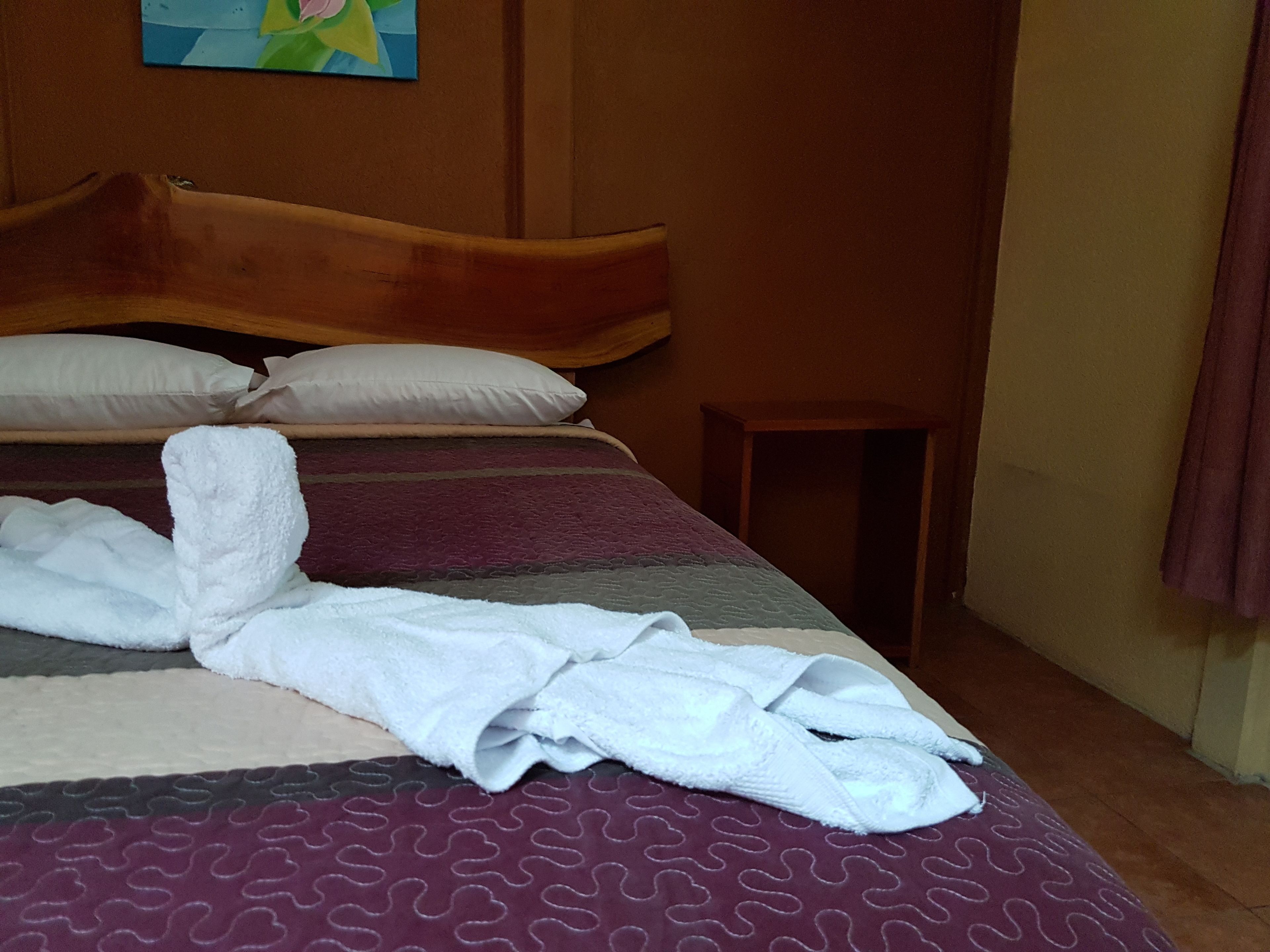 A neatly made bed with a patterned bedspread, a wooden headboard, and a small wooden stool beside it.