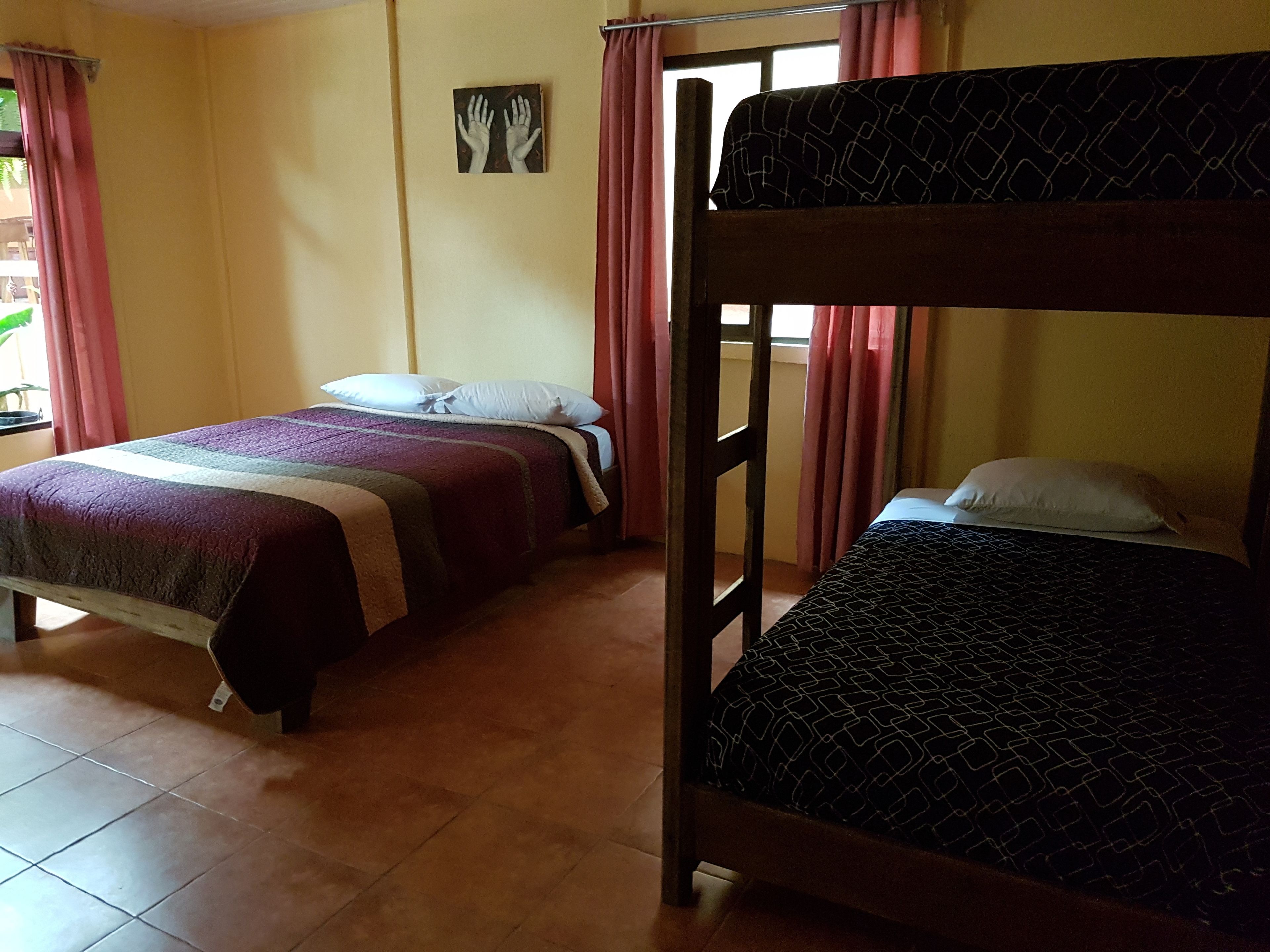 A dormitory room with two bunk beds, a bed with a patterned bedspread, and a wall-mounted artwork.