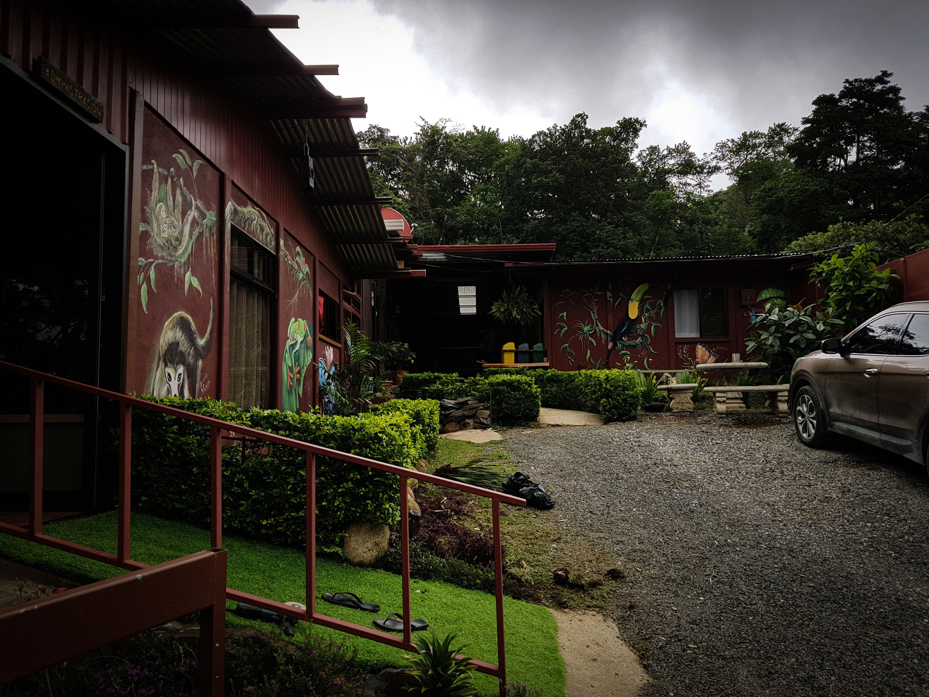 A building with a gravel driveway, a car parked outside, and a garden area with various plants and a bench.