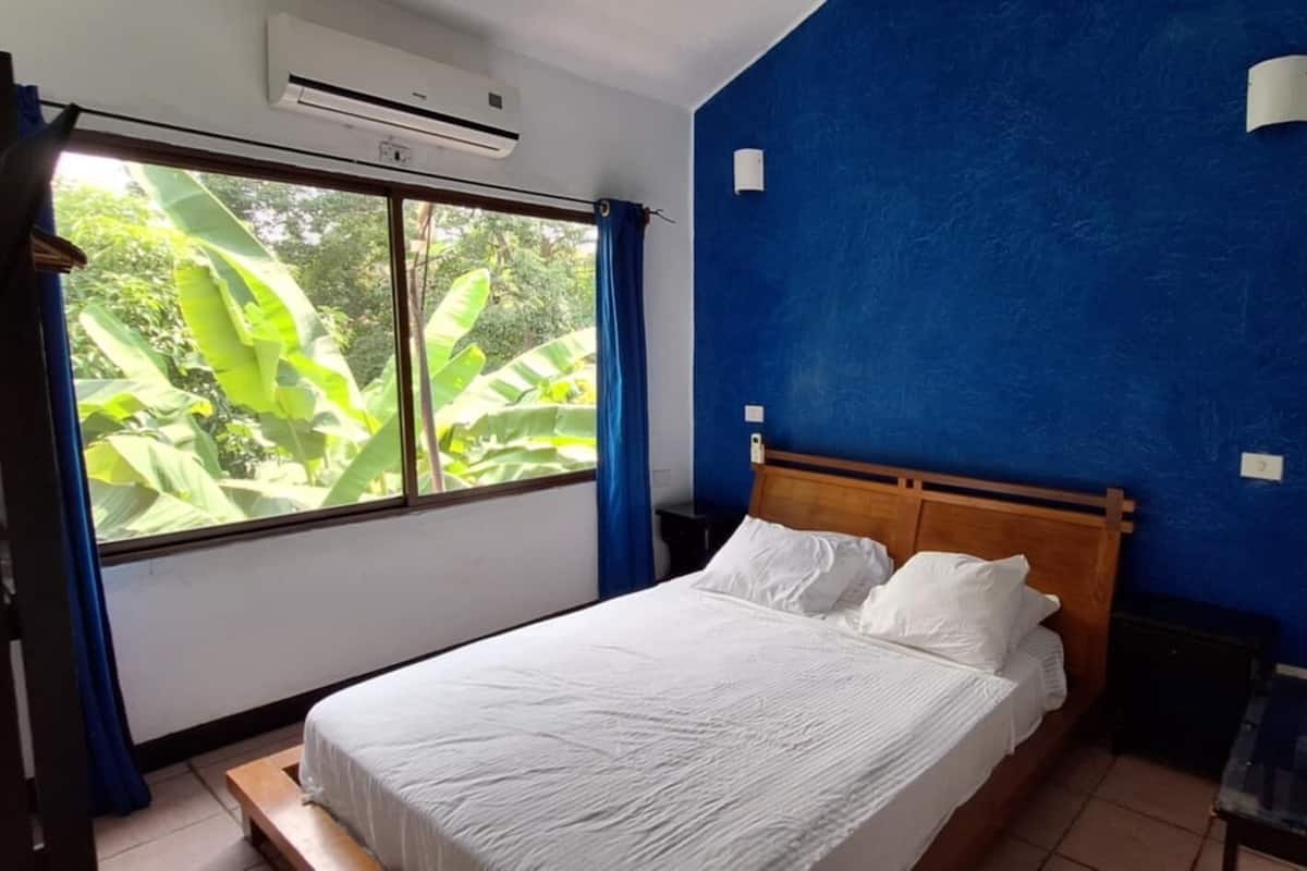 A bedroom with a bed, a window with curtains, and a blue wall.