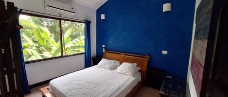A bedroom with a bed, a window with curtains, and a blue wall.