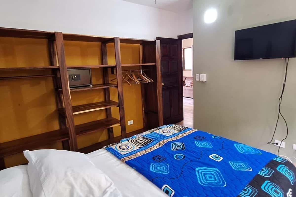 A bedroom with a bed, a wardrobe with multiple compartments, a television on the wall, and a bathroom visible through an open door.
