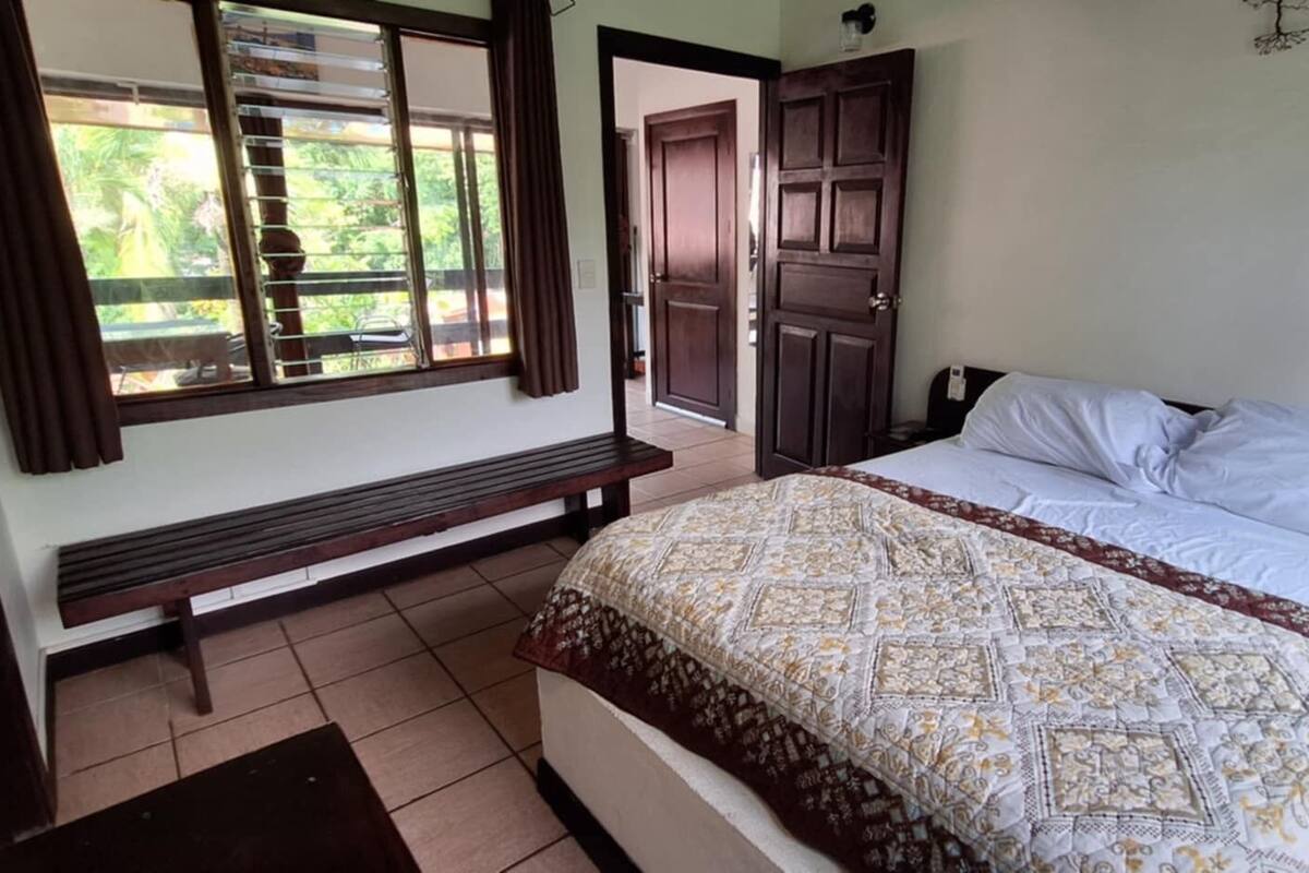A bedroom with a bed, a bench, and a window with blinds.