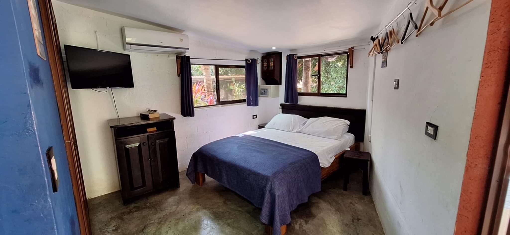 A bedroom with a bed, a TV, a wardrobe, and a window with curtains.