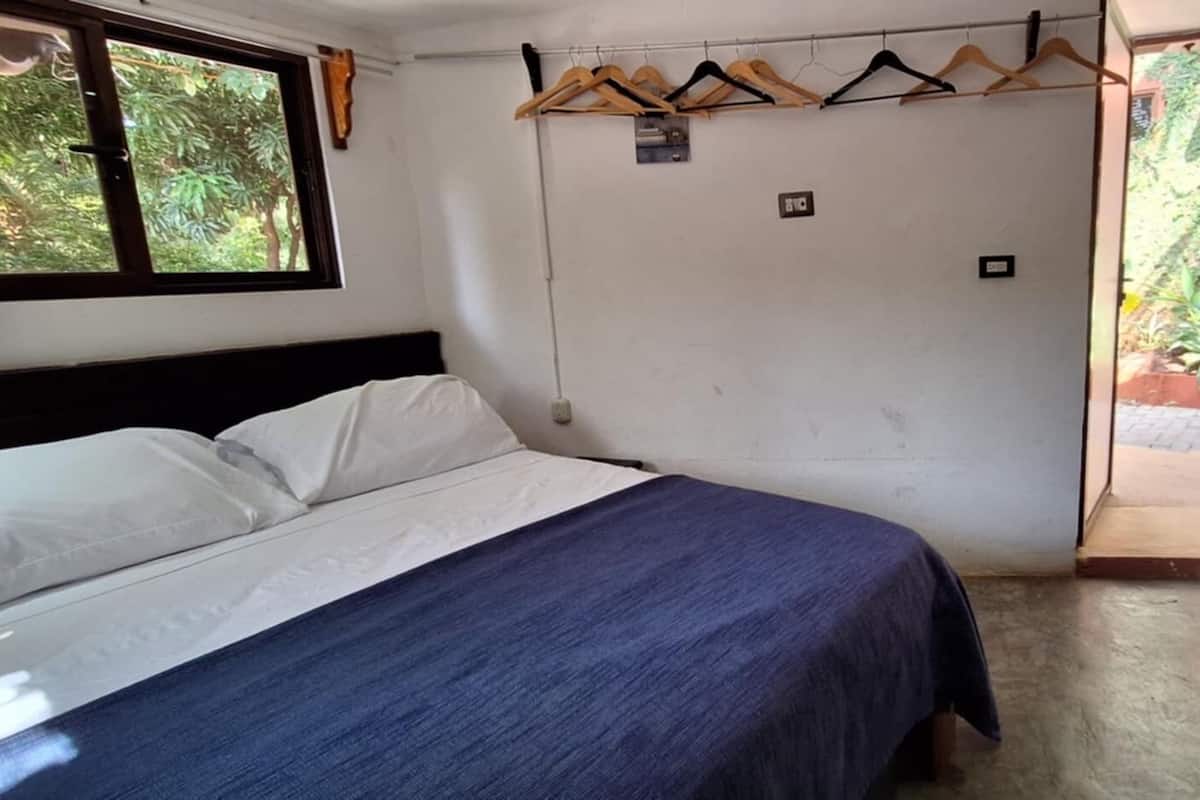 A bedroom with a bed, a wooden hanger rack, and a small stool.