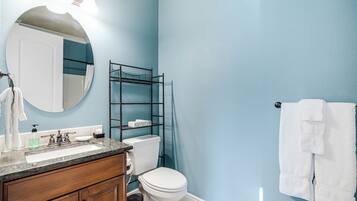 Un baño con pared azul, inodoro blanco, tocador de madera con lavamanos y un perchero para toallas.