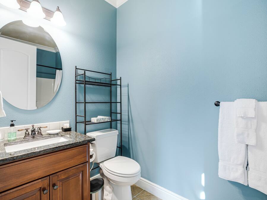 Un baño con pared azul, inodoro blanco, tocador de madera con lavamanos y un perchero para toallas.