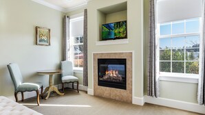 A room with a fireplace, a television mounted above it, a framed picture on the wall, and a view of the outdoors through large windows. - La Bastide Bed & Breakfast (Dundee)