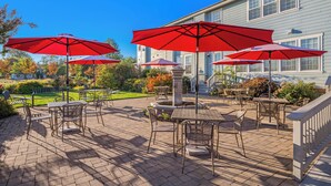 A patio with outdoor furniture and red umbrellas, a stone fountain, and a house in the background. - La Bastide Bed & Breakfast (Dundee)