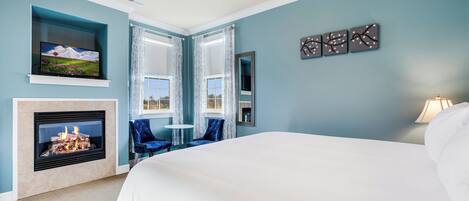 Une chambre à coucher avec un grand lit, une cheminée, un téléviseur et une vue sur l’extérieur par les fenêtres.