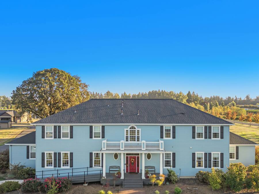 A two-story house with a balcony, a red door, and a well-maintained lawn.