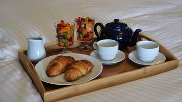 A tray with croissants, fruit salad, coffee cups, and a teapot on a bed.