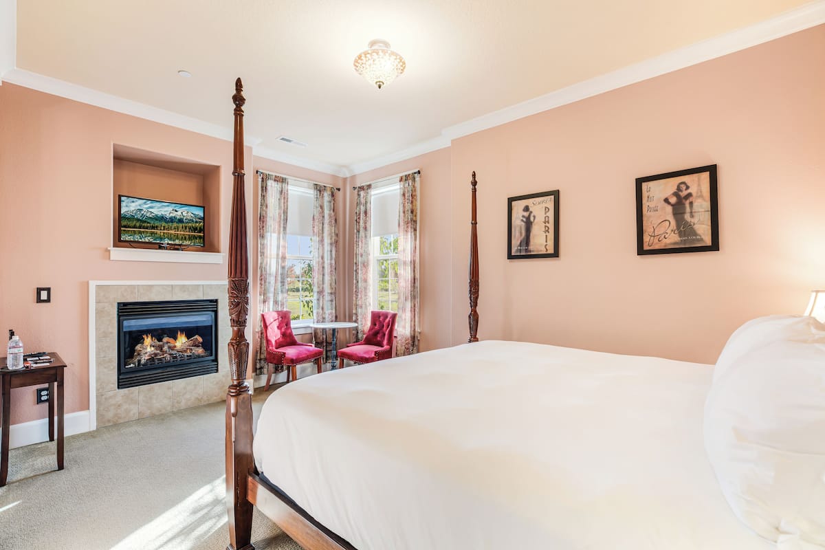 A bedroom with a four-poster bed, a fireplace, and two chairs.
