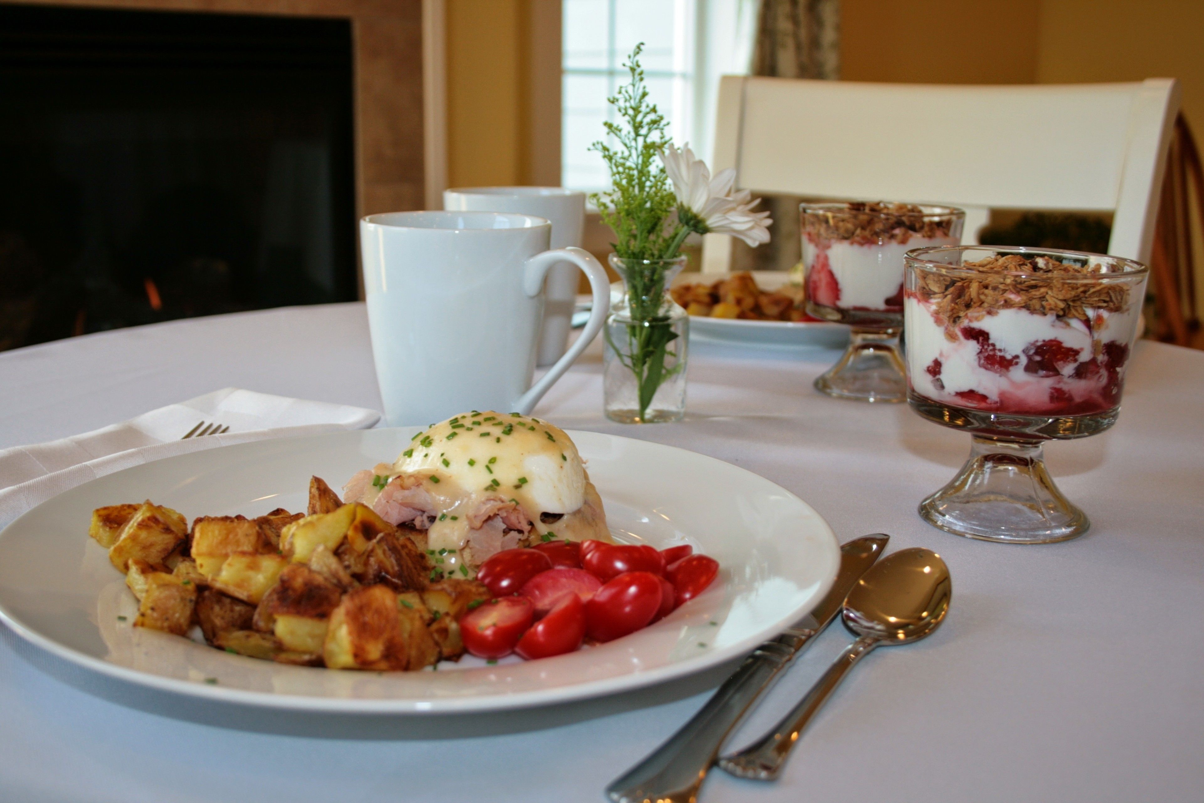 A breakfast setting with a plate of food, a cup, and a dessert on a table.