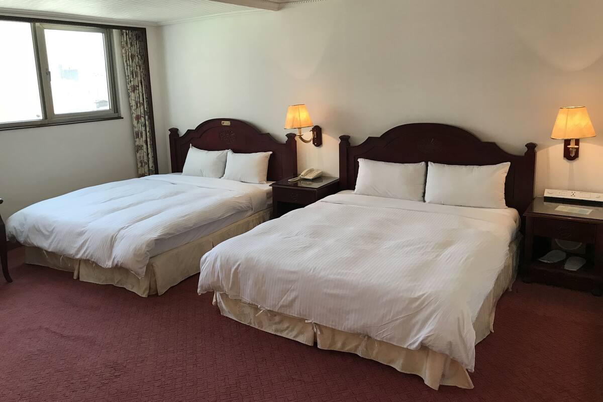 A hotel room with two beds, a window with curtains, and bedside lamps.