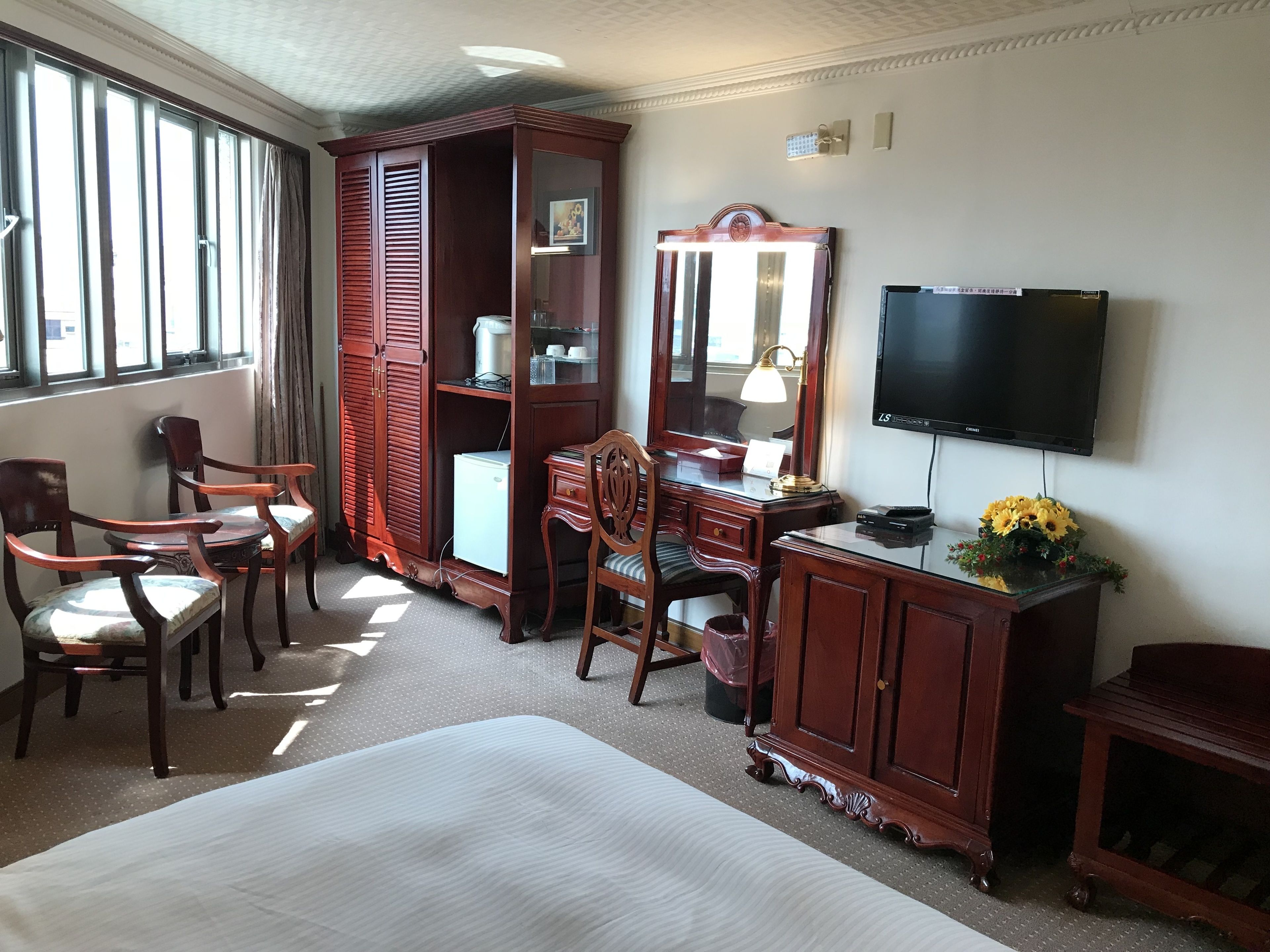 A hotel room with a bed, a desk with a lamp, a television, and a wardrobe.