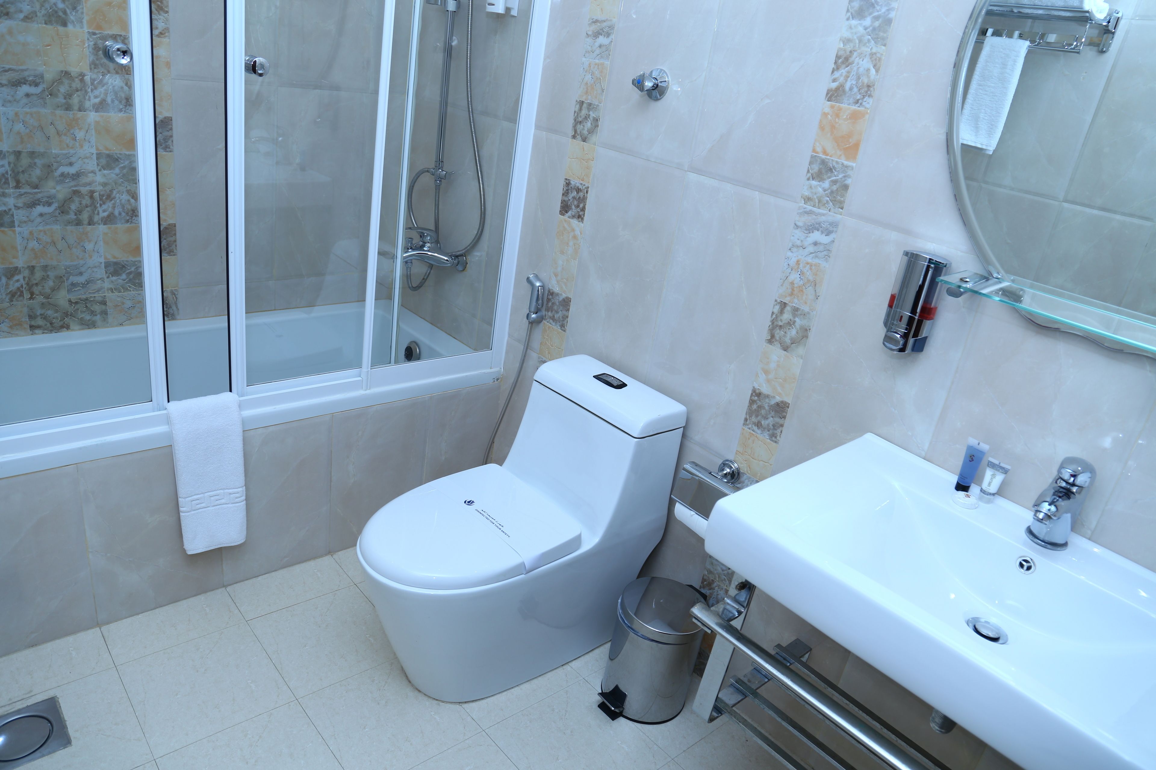 A modern bathroom with a glass-enclosed shower, a white toilet, and a sink with a glass shelf.