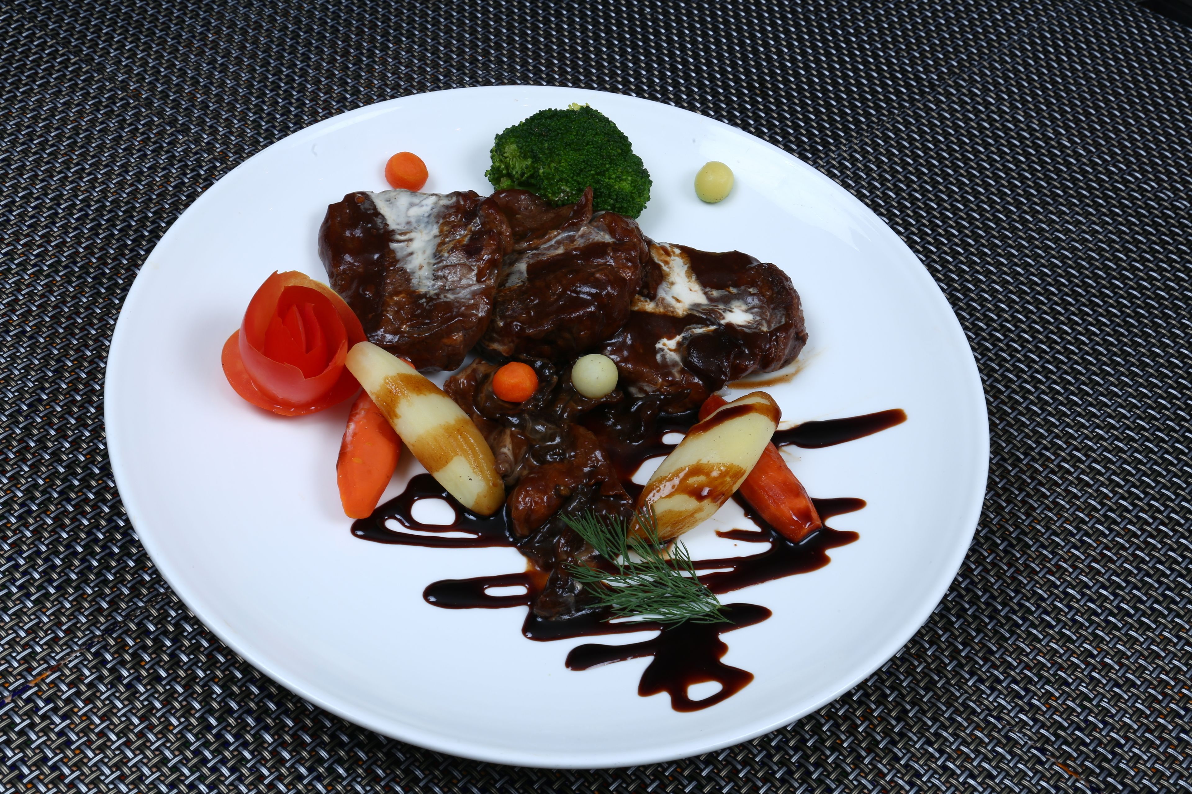 A plate of food with meat, vegetables, and sauce on a table.