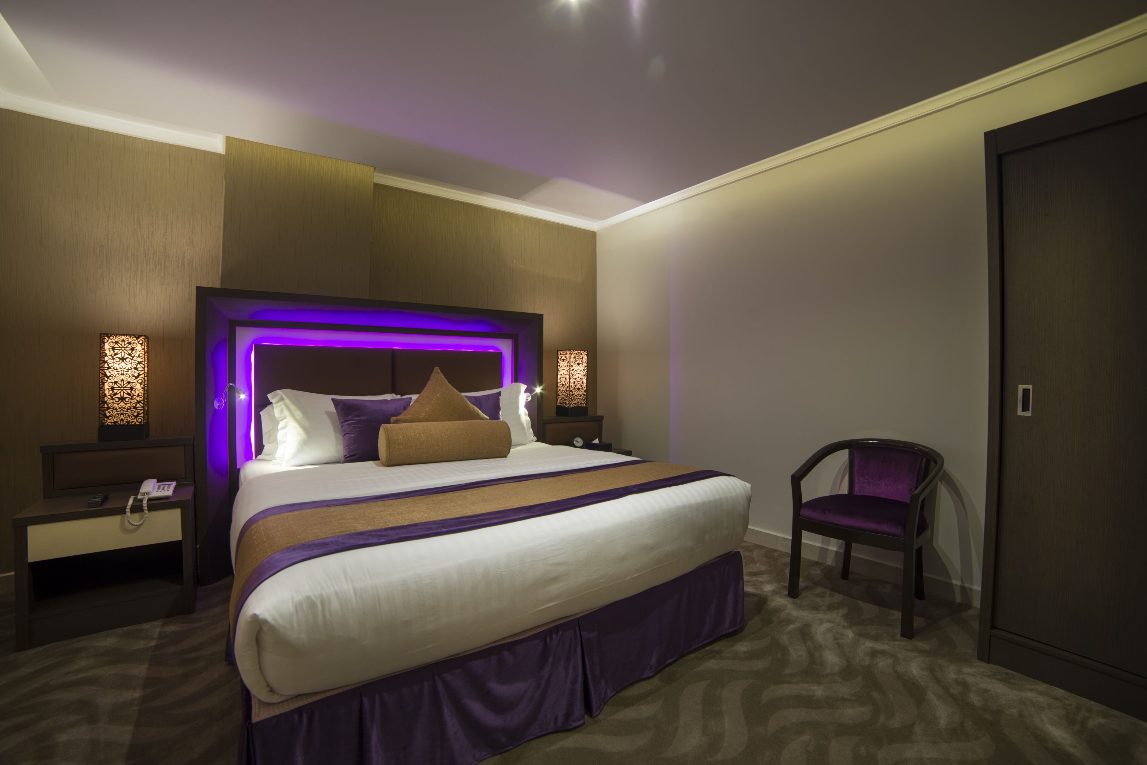 Una habitación de hotel moderna con una cama grande, una mesita de noche con teléfono, una silla y un armario.