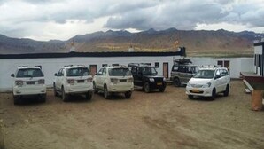 A parking area with several vehicles, including SUVs and a truck, parked in front of a building with a mountainous backdrop.