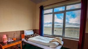 A room with a bed, a small table with a lamp, and a window with a view of a landscape.