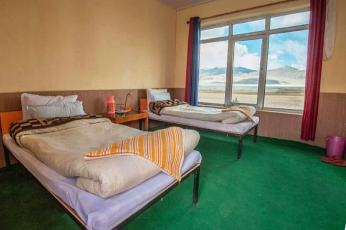 Una habitaci ón con dos camas, un ventanal con vistas a las montañas y una alfombra verde.