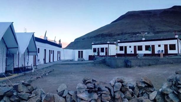 A row of simple, white buildings with flat roofs, set against a hilly backdrop.