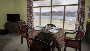 Zona pranzo con tavolo apparecchiato per quattro persone, televisione e vista su un lago con montagne sullo sfondo.