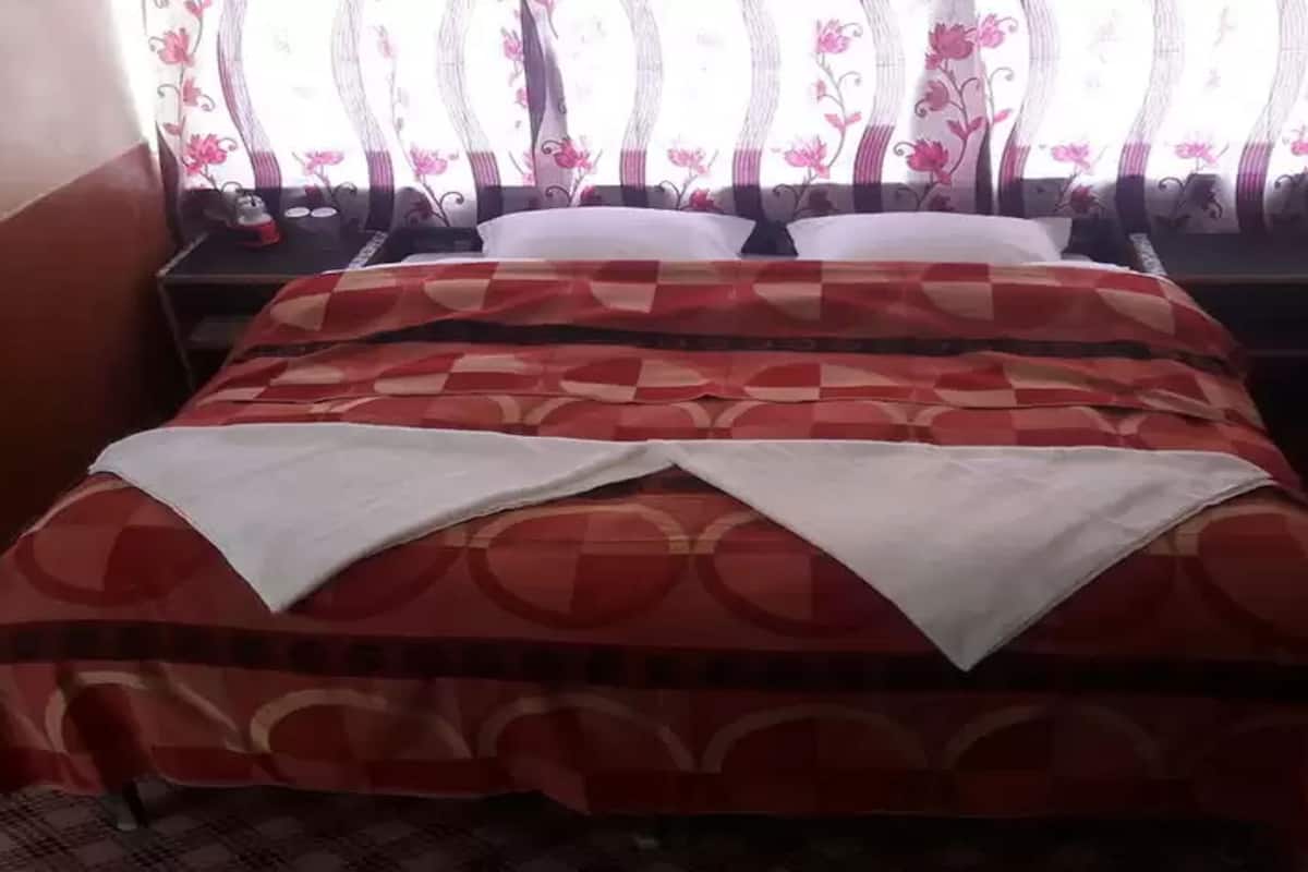 Una cama con una colcha estampada, un almohadón blanco y una mesita de noche con una lámpara.