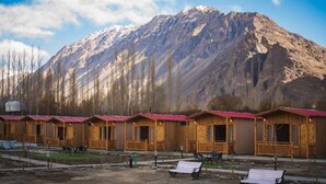 Una fila di cabine di legno con tetti rossi, ciascuna con una finestra e una porta, sullo sfondo di una montagna innevata.