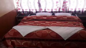 Un letto con una coperta a motivi rossi e bianchi, due cuscini bianchi e una finestra con tende floreali.
