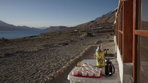 Un tavolo con tazze e un thermos su un balcone con vista sulla spiaggia e sulle montagne.