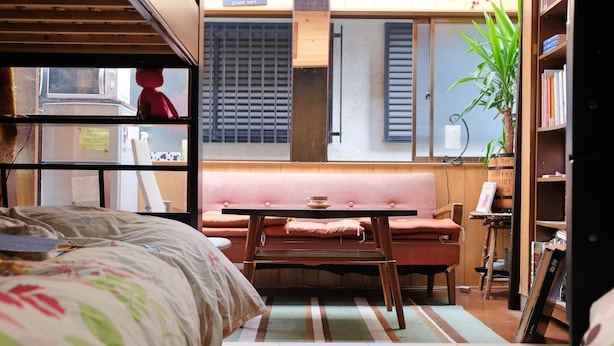 A cozy room with a bed, a pink sofa, a small table, and a bookshelf. - Kimono Inn Utakata - Hostel (Himeji)