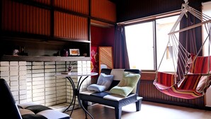 A cozy room with a sofa, a small table, a hanging chair, and a brick wall. - Kimono Inn Utakata - Hostel (Himeji)