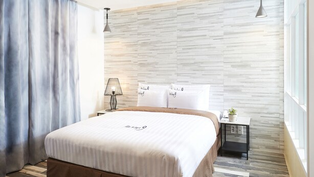 Een moderne hotelkamer met een groot bed, een nachtkastje met lamp en uitzicht op de stad door grote ramen.