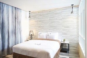 Et moderne hotelværelse med en stor seng, et natbord med lampe og udsigt over byen gennem store vinduer.