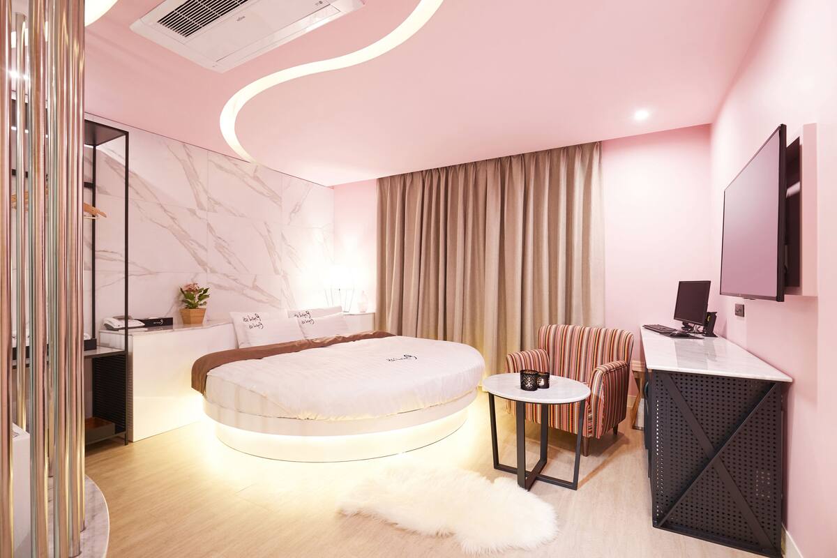 Un dormitorio moderno con una cama redonda, un escritorio, una silla, una mesita pequeña y un televisor.