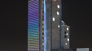 Een hotel met een opvallend 'HOTEL'-bord bovenop, een verticale gevel met verlichte strepen en een deel met ster-vormige lampjes.