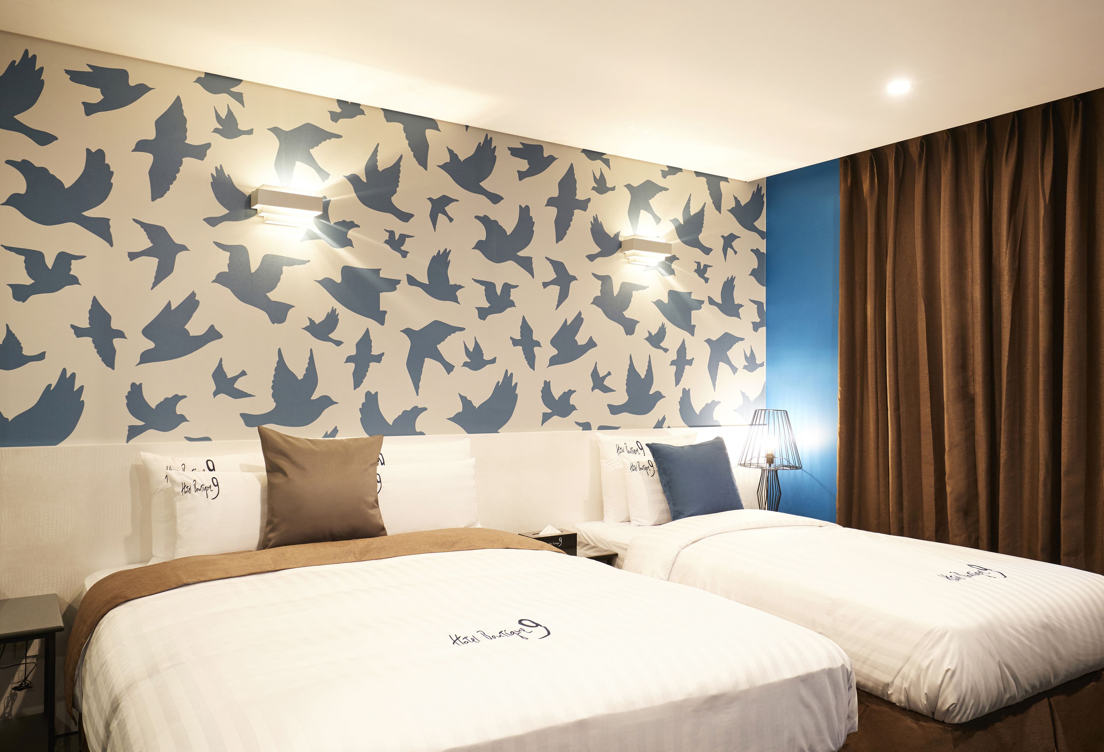A hotel room with two beds, a wall with bird patterns, and a curtain.