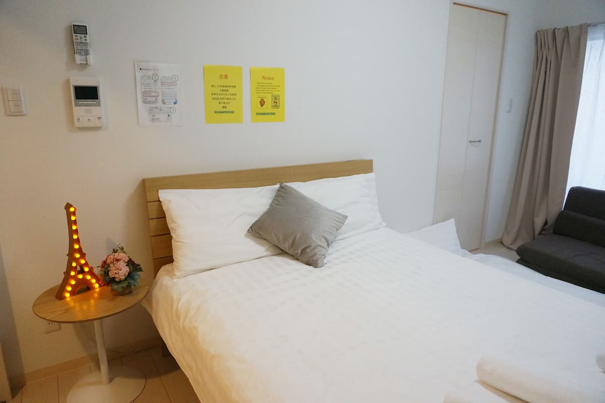 Een hotelkamer met een bed, nachtkastje met lamp, stoel en een deur.