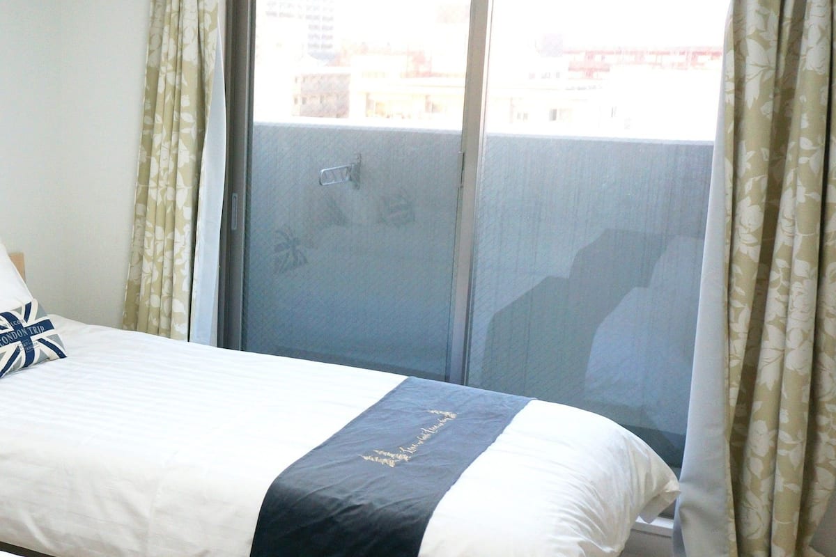 Een hotelkamer met een bed, een raam met gordijnen en uitzicht op gebouwen.