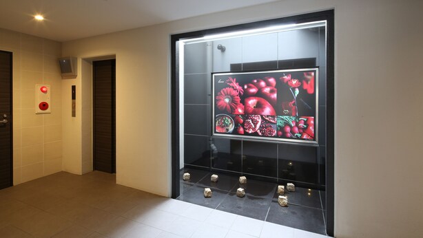 A modern hallway with a digital display showing floral patterns, a red emergency light, and a set of small cubes on the floor.