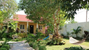 A house with a red roof, a front door, and a small garden with a hammock and a slide. - Celvis Vacation Cottages (Panglao)