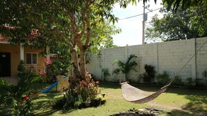 A hammock in a grassy backyard with a brick wall, a play structure, and various potted plants. - Celvis Vacation Cottages (Panglao)