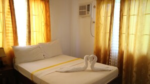 A hotel room with a neatly made bed, a bedside table with a lamp, and a wall-mounted air conditioning unit. - Celvis Vacation Cottages (Panglao)