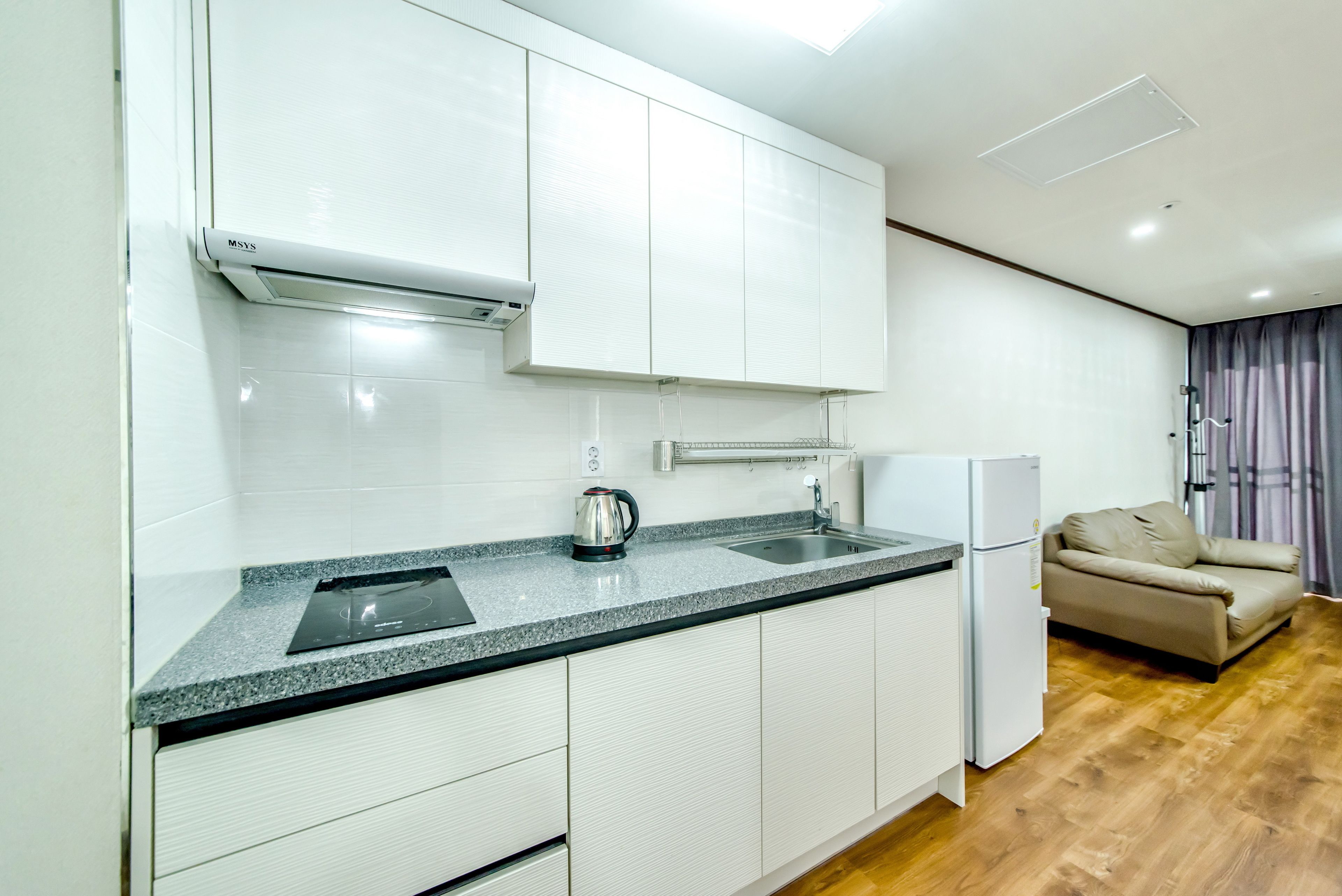 A modern kitchen with white cabinets, a granite countertop, a built-in oven, and a refrigerator.