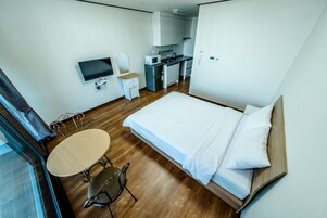 A compact hotel room with a bed, a small table with chairs, a TV, a microwave, and a kitchenette.