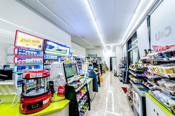 A brightly lit convenience store with self-service checkout machines, shelves stocked with snacks and beverages, and a clean, tiled floor. - Rejina Pension (Seogwipo)